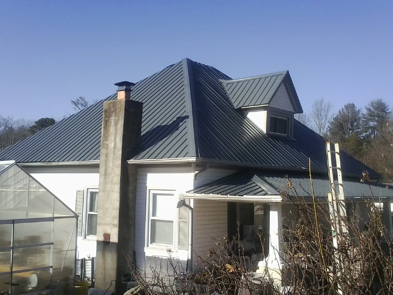Dark blue standing seam metal roof on a white farmhouse with dormer — Slate & Tile Roof Repair by Roofing Brothers in Saint Leonard