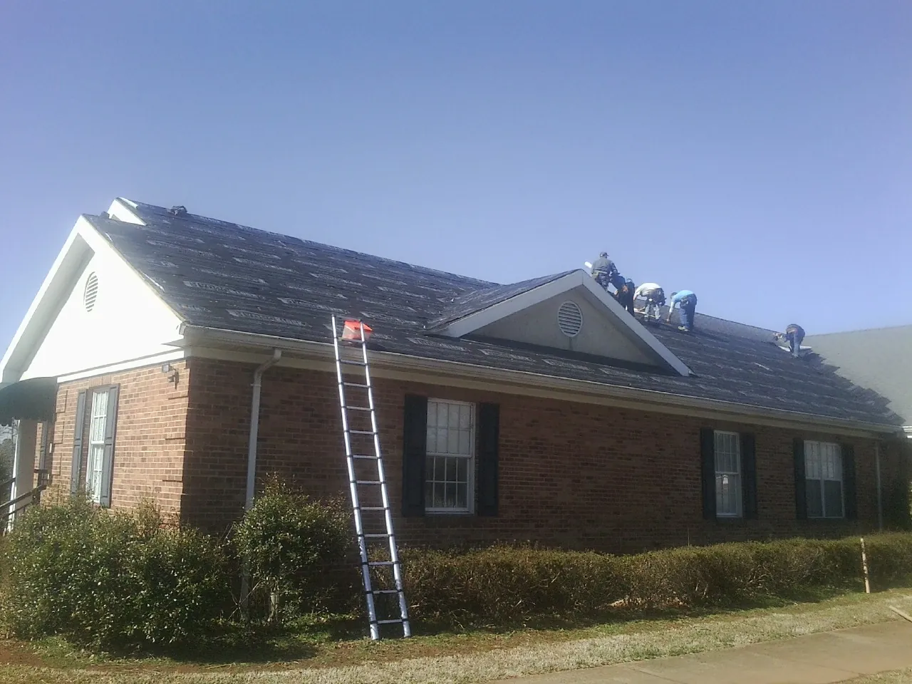 Crew tearing shingles off a brick ranch roof with a ladder set — Emergency Roof Repair work by our crew in Saint Leonard