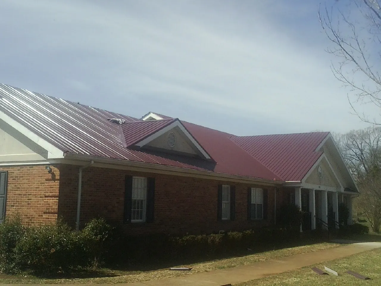 Red metal roof with gabled entries on a long brick building, from a Hail Damage Roof Repair job in Saint Leonard