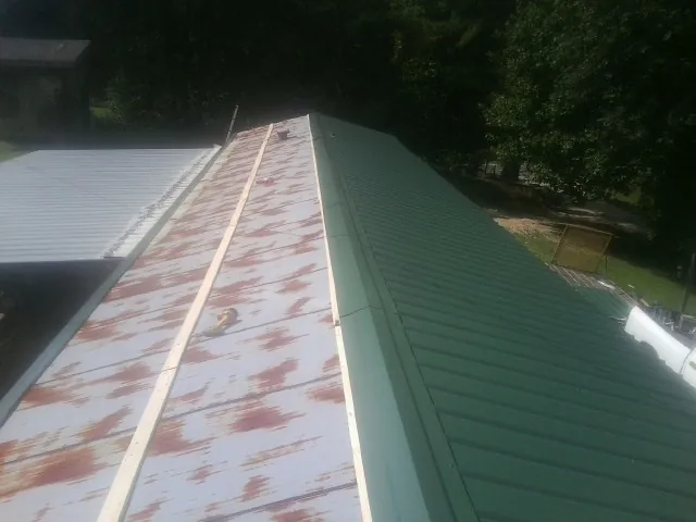 Old rusted panels beside newly installed green metal roofing — Wind Damage Roof Repair by Roofing Brothers in Saint Leonard
