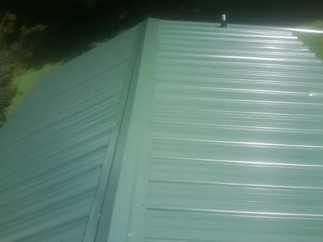 New green metal panels meeting at the ridge of a roof — Flat Roof Repair work by our crew in Saint Leonard
