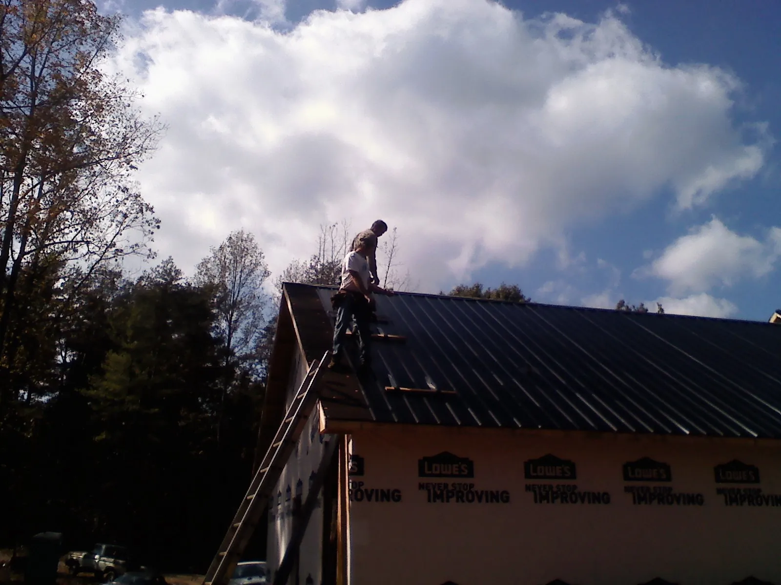 Roofer fastening dark metal panels high against a cloudy sky, from a Roof Inspection job in Saint Leonard