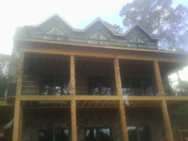 Dormers and porch framing on a large log home under construction — Roof Coating work by our crew in Saint Leonard