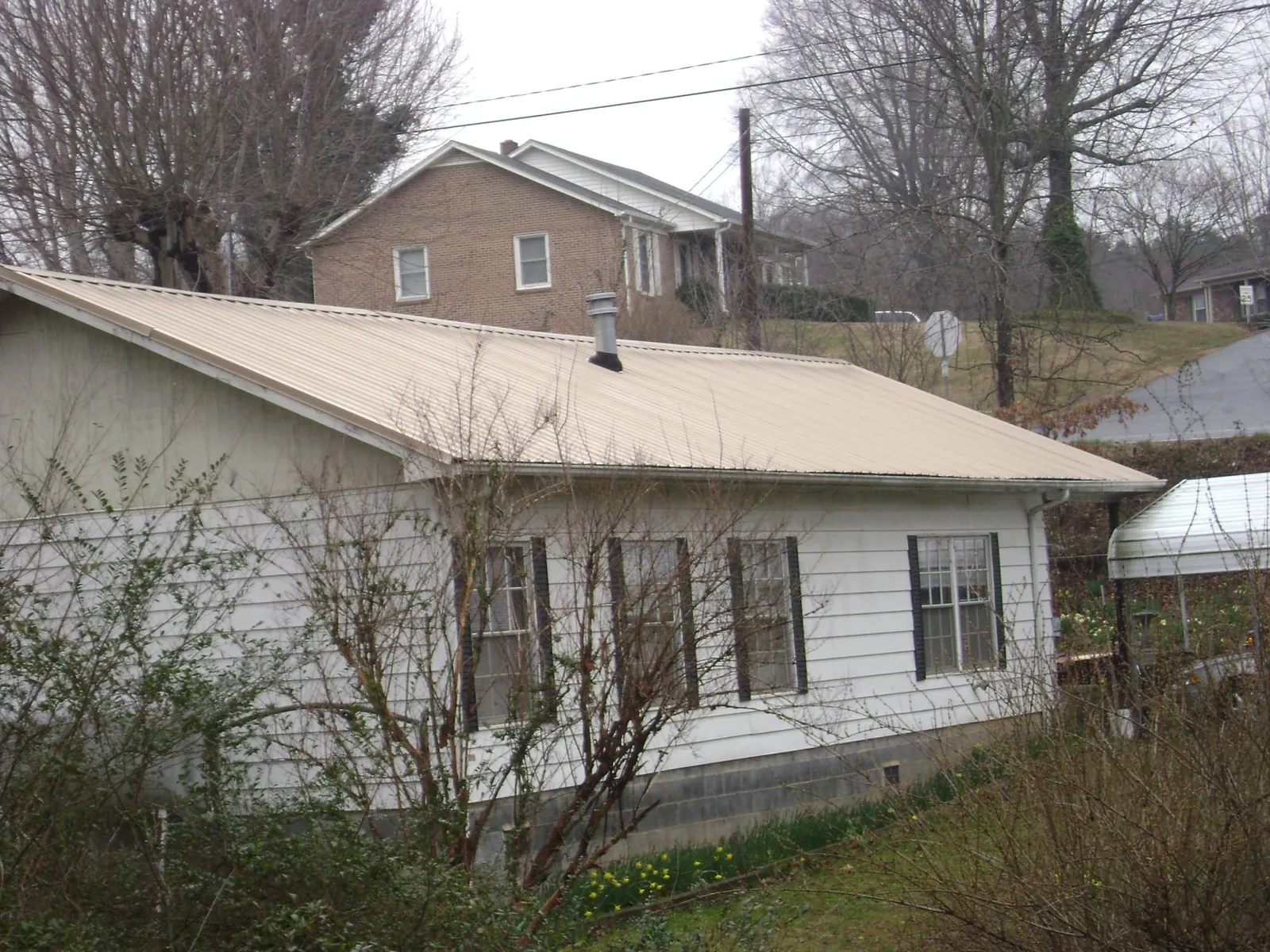 Tan metal roof on a white sided house set into a hillside — Commercial Roofing by Roofing Brothers in Saint Leonard